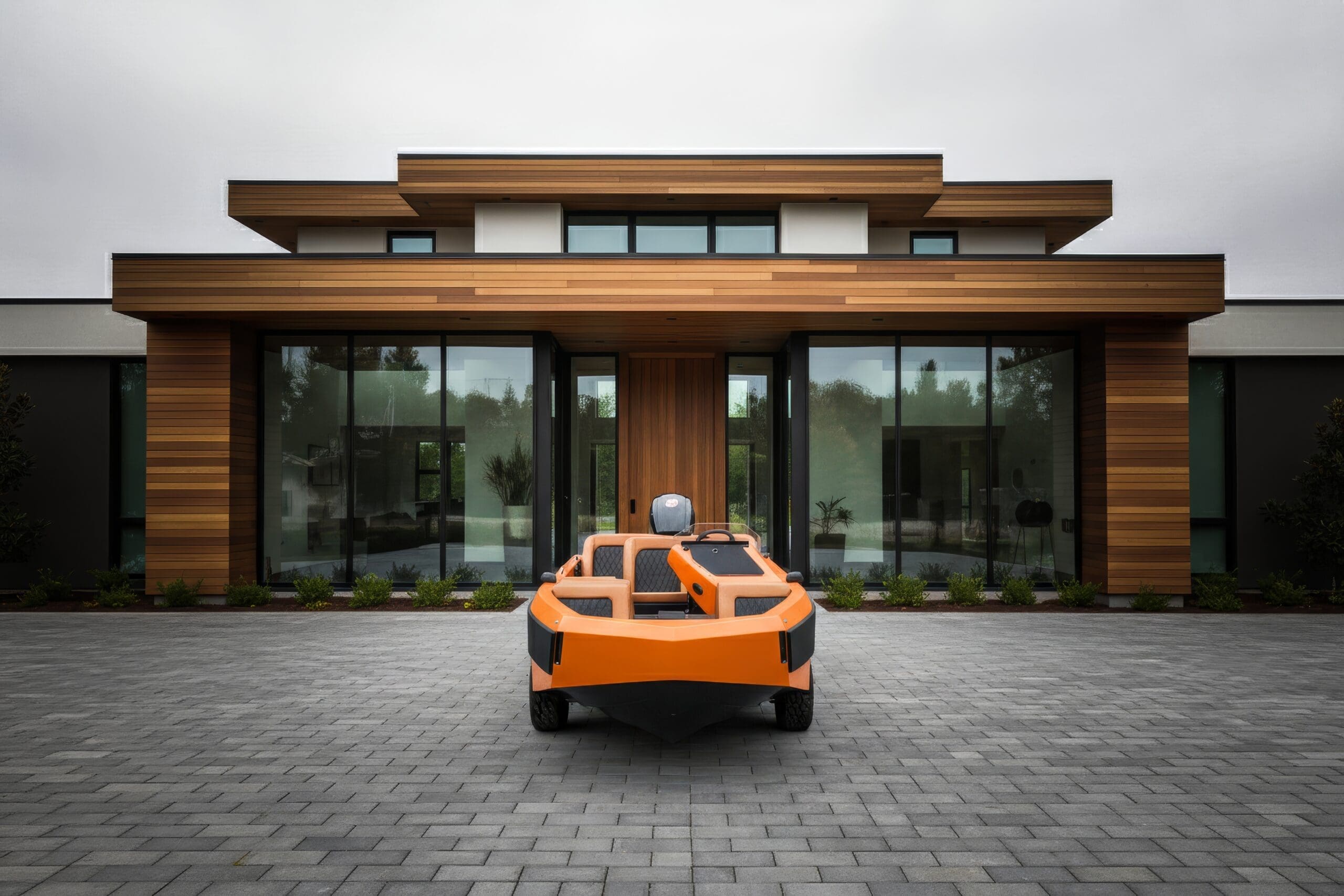 a orange steel Amphibious car parked at front of a luxury glass house